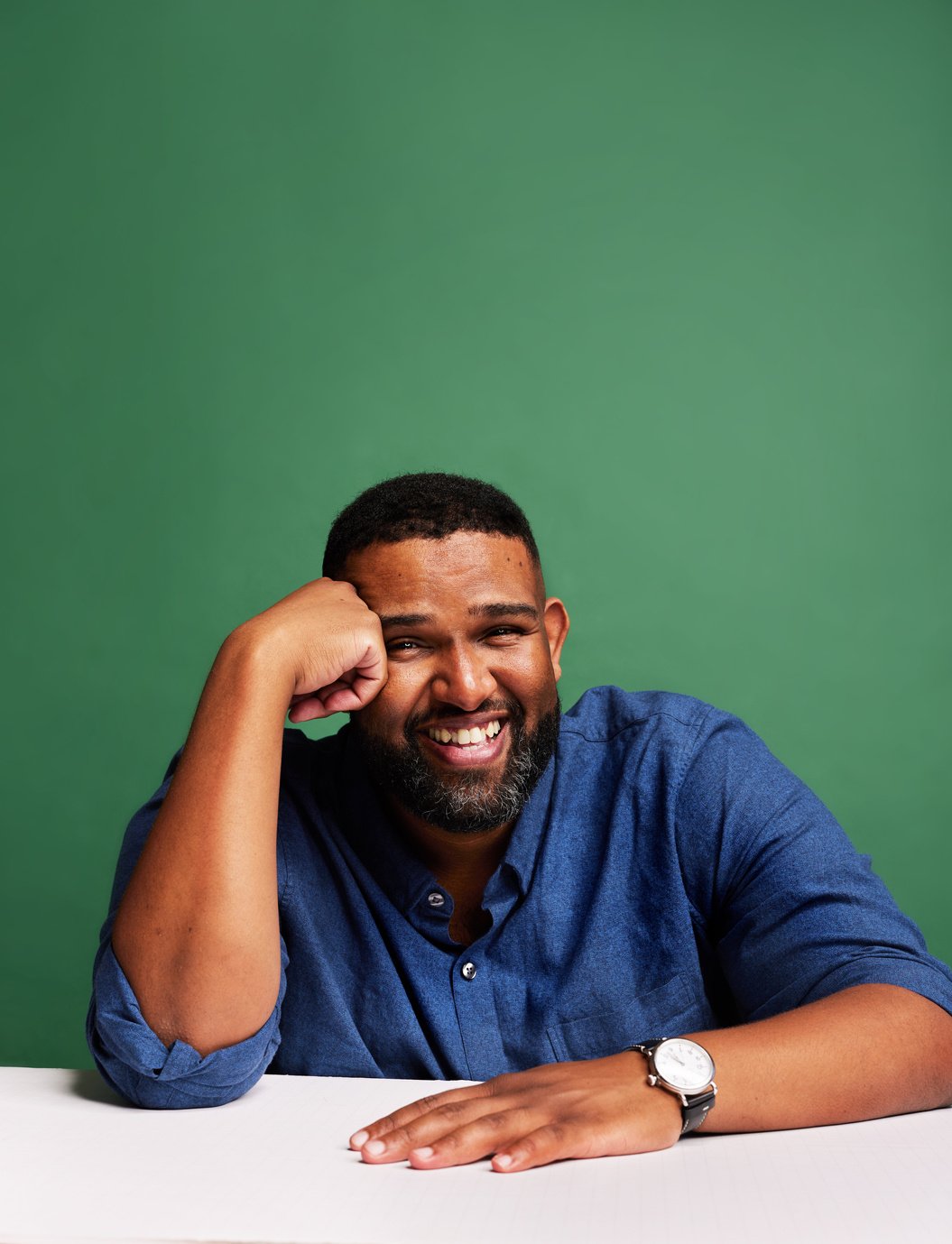 a smiling person in a blue shirt sitting in front of a green background